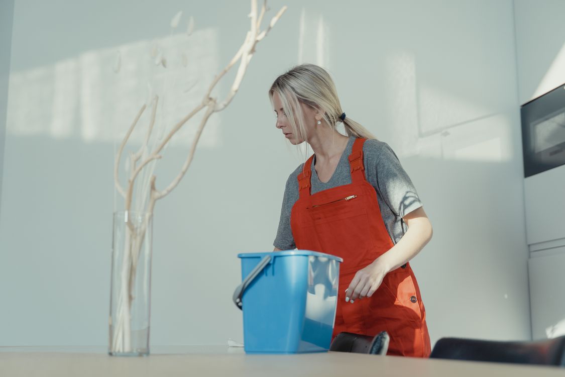 Professional cleaner in orange apron with bucket cleaning a bright home interior